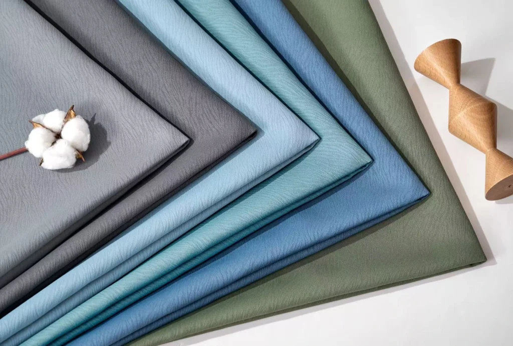 Close Up Texture Of Folded 85% Blackout Curtain Materials In Blue, Grey, And Green. Factory Direct Supply In Bulk Rolls With 280Cm To 320Cm Seamless Width.